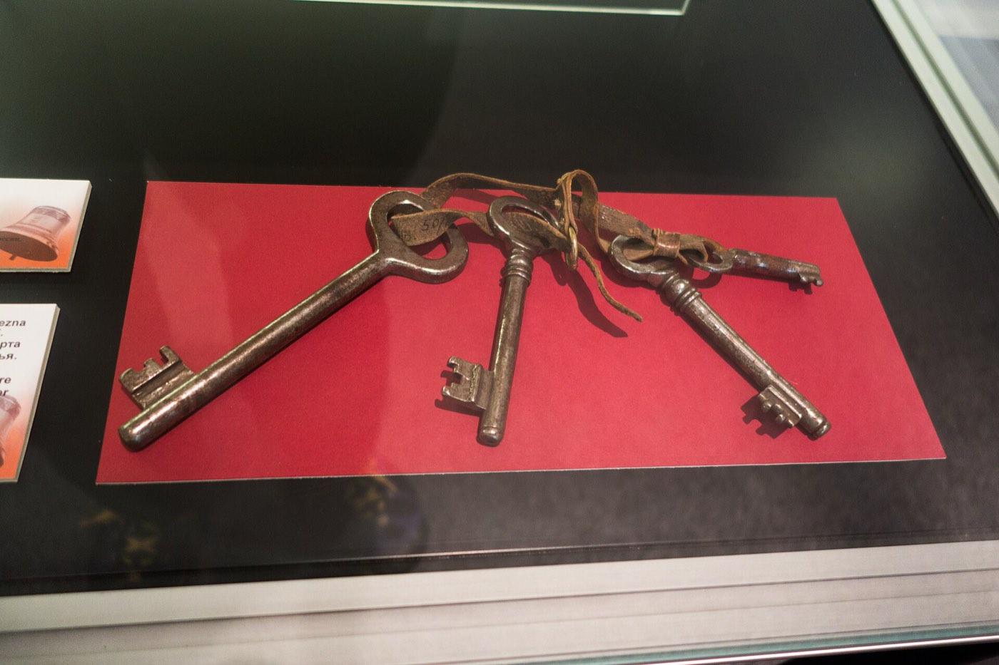 Three old iron keys on a leather strap, lying on red card in a museum case
